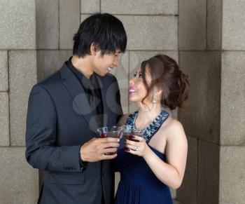 Closeup photo of young adult couple sharing a drink, as they look at each other, with stone wall in background 