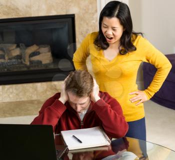 Photo of mature couple, with woman yelling at man, while working from home with fireplace and partial sofa in background  
