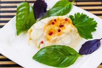 Closeup horizontal photo of baked stuffed sole fish, red peppercorn, sweet basil, inside white square plate on bamboo place mat 