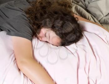 Young girl too tired to wake up in the morning while lying face down in bed