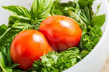 Tilted closeup horizontal photo of a two joined tomatoes, basil and parsley in white bowl