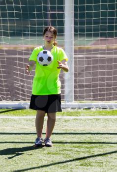 Vertical photo of young girl dropping soccer ball just before kicking it with posts and net in background 