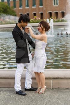 Vertical photo of young adult man kissing his lady hand with water fountain, geese and brick building in background 