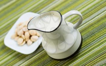 Angled horizontal photo of almond milk in pitcher with fresh almonds, in a white dish, with green table cloth in background 