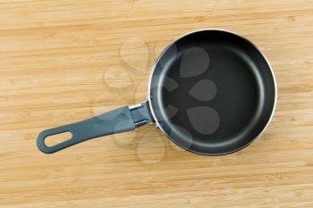 Horizontal photo of new gray and black frying pan on natural bamboo wood