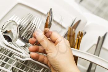 Horizontal photo of female hand examining stainless steel spoon for cleanliness from the dishwasher 
