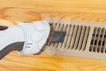 Horizontal photo of vacuum cleaning heater floor vent with Red Oak Floors in background 