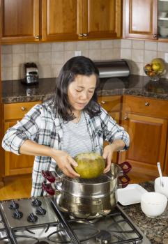 Vertical photo of mature woman lifting winter melon, from steaming pot, with both hands to place on white dinner plate