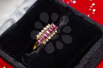 Horizontal photo of gold ring containing precious stones and diamonds sitting inside of Jewelry box on red background 