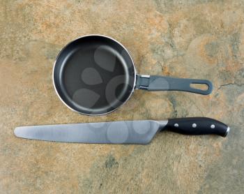 Photo of large serrated knife and frying pan on natural stone counter top 
