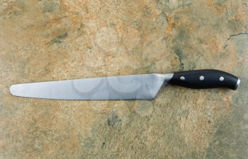 Horizontal photo of large serrated knife on natural stone counter top 