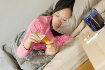 Horizontal photo of mature woman holding medicine container while lying in bed sick