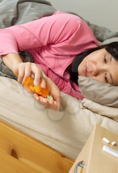 Vertical photo of mature woman opening medicine container while lying in bed sick