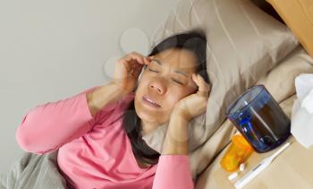 Horizontal photo of mature woman holding her head in pain while lying in bed sick
