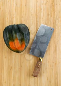 Vertical photo of single large acorn squash with butcher knife on natural bamboo cutting board