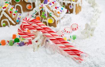 Horizontal close up photo of holiday candy canes with Gingerbread houses surrounded by powdered  snow in the background 