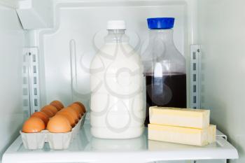 Horizontal photo of milk, eggs, butter and juice on glass shelf inside of refrigerator