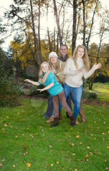 Vertical photo of family dancing in front of trees, with sunlight coming through, during a nice day in the fall season
