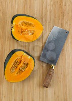 Vertical photo of half cut large acorn squash with butcher knife on natural bamboo cutting board