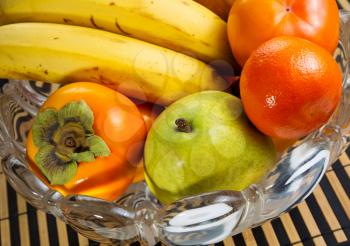 Photo of fresh fruit, in a glass bowl, consisting of oranges, bananas, and pears with bamboo place mat underneath