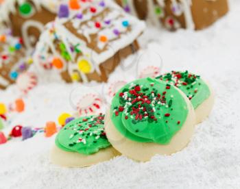 Close up photo of frosted sugar Christmas cookies with Gingerbread houses surrounded by powered snow in the background 