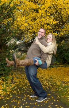 Vertical photo of happy adult couple with husband giving his wife a piggy back ride in the park during a nice day in the autumn season 