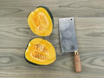 Photo of large acorn squash cut in half with butcher knife on aging white ash wood 