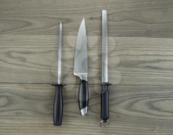 Photo of single large kitchen knife and two sharpeners on aged white ash wood