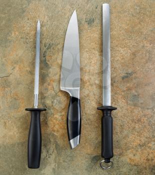 Photo of single large kitchen knife and two sharpeners on natural stone
