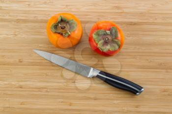 Horizontal photo of dry fresh persimmons with single knife lying on natural bamboo wood