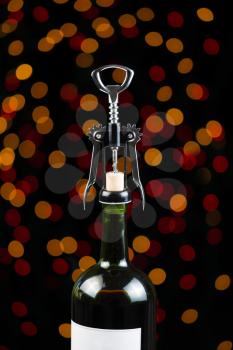 Vertical photo of Red Wine bottle and metal hand opener on top of cork with holiday lights in the background