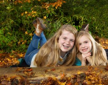 Horizontal photo of two sisters having fun while lying on the ground in the park on a nice autumn day