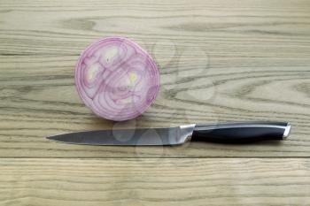 Horizontal photo of sliced purple onion with single knife lying on aged white ash boards