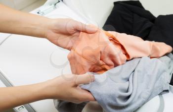 Photo of female hands taking the dry laundry out of the dyer 