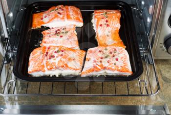 Horizontal photo of Baked Wild Red Salmon pieces coated with dried red peppercorns and sea salt inside oven with stone counter top underneath 