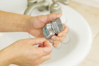 Horizontal photo of female hands pulling dental floss out of small silver container in bathroom with sink and counter top in background 