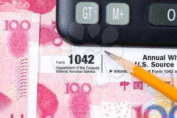 Horizontal photo of partial IRS Income tax form 1042, for Foreign Income, pencil and calculator with Chinese Currency in background 