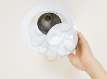 Photo of brand new flood light bulb being held by female hand with recessed ceiling light mount in background 