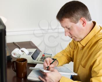 Photo of mature man, recording data from the computer, working on his taxes with tax booklet and pencil in hands 