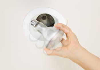 Photo of burned out flood light bulb being held by female hand with recessed ceiling light mount in background 