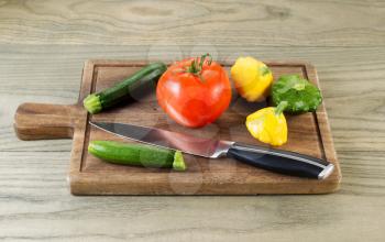 Horizontal photo of fresh raw baby squash, tomato and knife on black walnut board with aged wood underneath