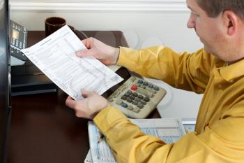 Horizontal photo of mature man pulling, with focus on tax worksheet, tax forms from printer 