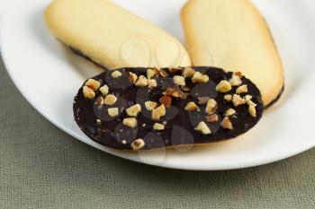 Horizontal photo of dark rich chocolate cookies and nuts on white plate with textured table cloth underneath
