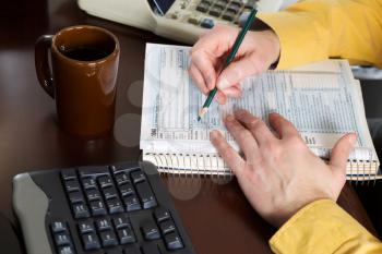 Horizontal photo with focus on male hands working on tax table forms and other office equipment on desk top