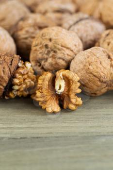 Close up vertical photo of unshelled half of walnuts lying on faded wood with additional nuts both shelled and unshelled in background 