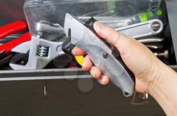 Horizontal photo of female hand taking out box cutter from used toolbox 