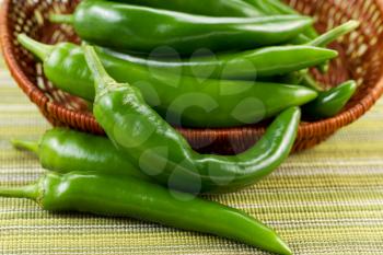 Closeup horizontal photo of fresh Korean Green Peppers falling out of basket with textured table cloth underneath
