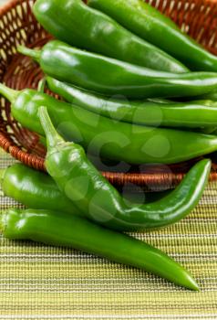Closeup vertical photo of fresh Korean Green Peppers falling out of basket with textured table cloth underneath

