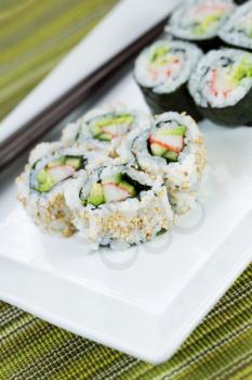 Closeup vertical photo of freshly handmade sushi rolls in white plate and chop sticks in background with texture green cloth underneath 