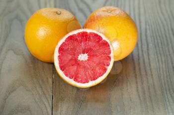 Horizontal photo of sliced ruby red grapefruit half in front of two whole fruits on aged wood
